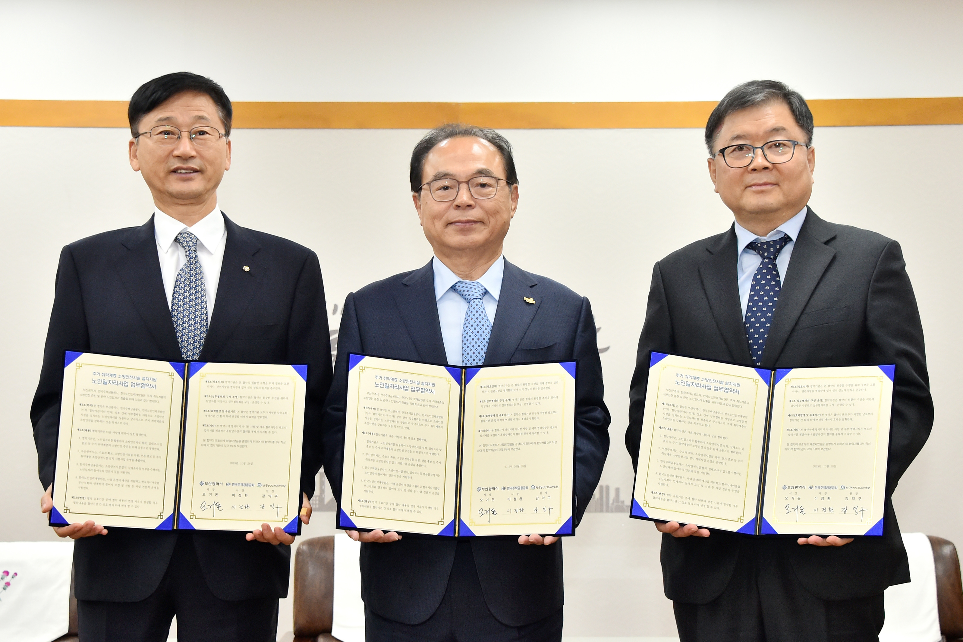 한국노인인력개발원 강익구 원장과 부산광역시 오거돈 시장, 한국주택금융공사 이정환 사장이 업무 협약서를 들고 정면을 바라보며 서있는 모습